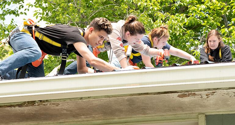 Several students wearing a harness and working on a roof.